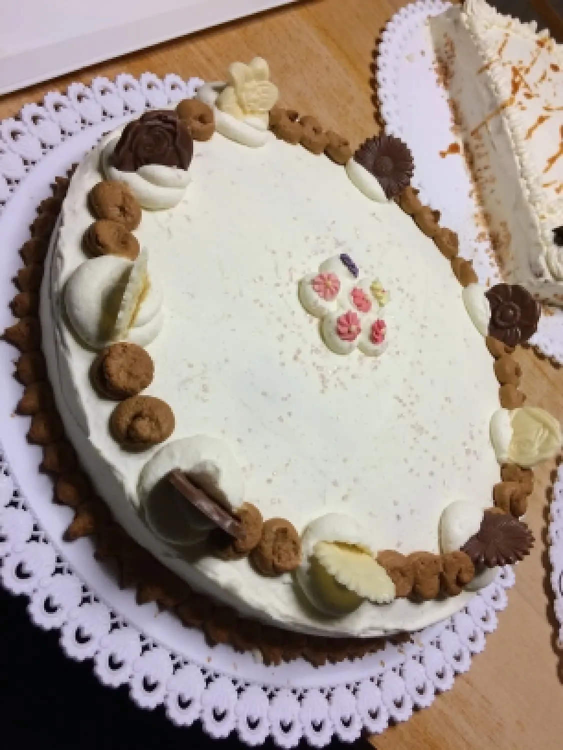 Grand gâteau ovale à la crème café, bordé de biscuits et de fleurs en chocolat