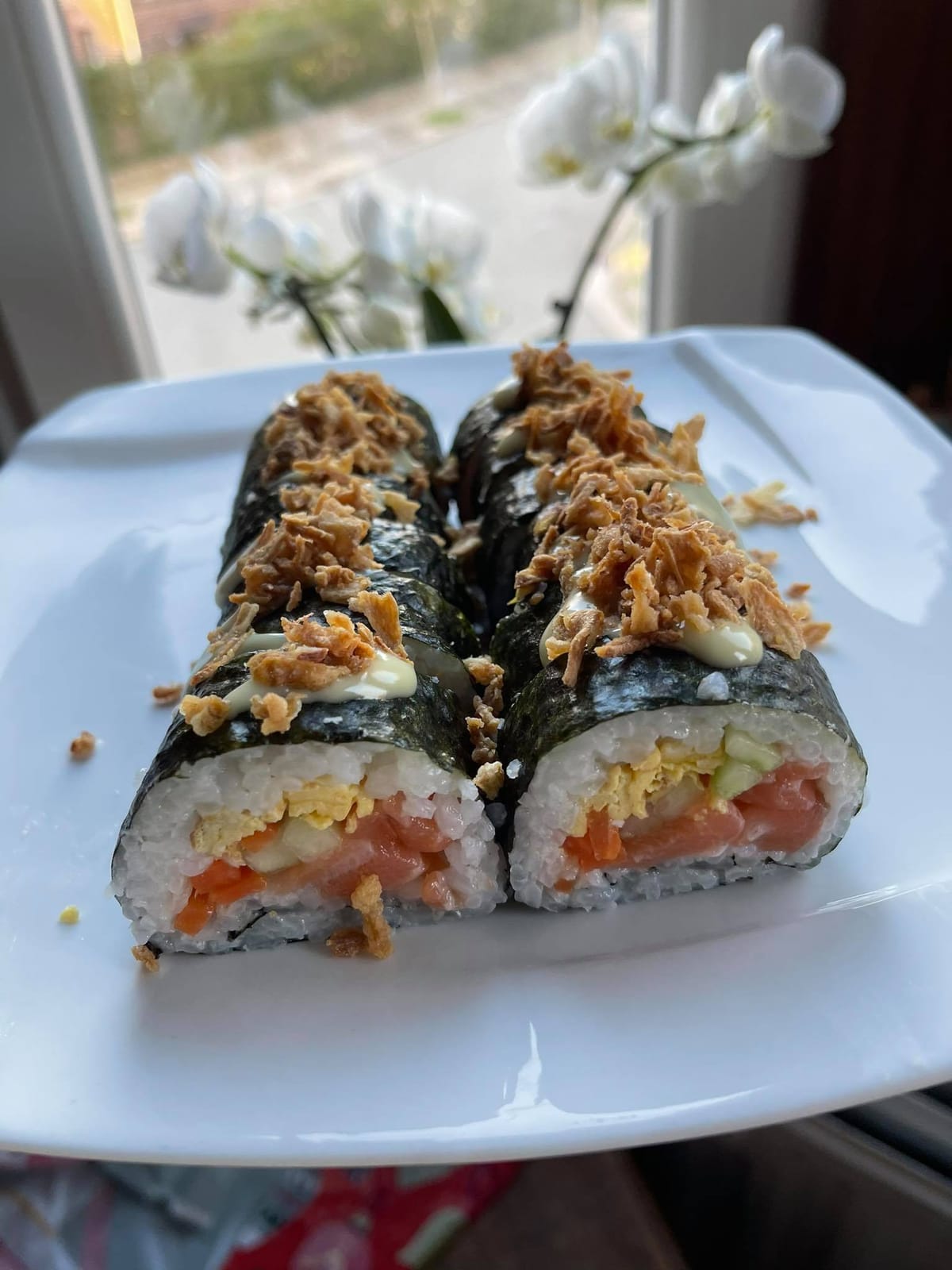 Makis au saumon garnis d'oignons frits, dressés sur une assiette